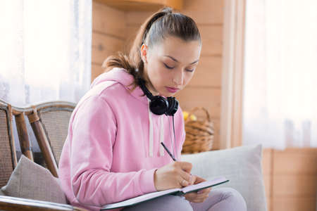 Young beautiful millennial woman in casual wear studying at home, draws sketch, writing notes in...