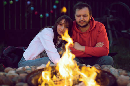 Portrait of the happy lovely couple sitting by fire on autumn night. Relaxing near the fire in the...