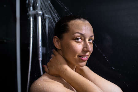 Portrait of smiling nude young woman enjoying flowing water, taking shower, standing in bathroom...