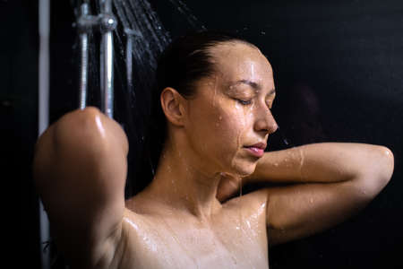 Pretty girl washing her body taking shower closing eyes with drops of water running down her wet skin.の写真素材