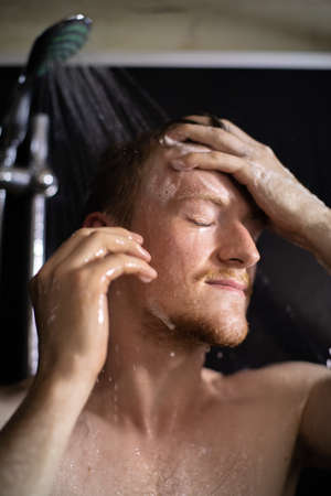 Close up sensual portrait of young beautiful  man taking shower in black bathroom, happy sexy guy...