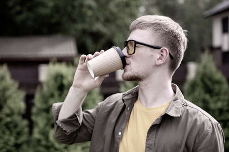 Portrait of young bearded guy in yellow glasses and yellow t-shirt casually dressed sipping coffee...