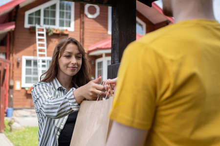Happy beautiful woman customer receiving order from delivery man in front of house, Express delivery, Online delivery service concept, delivery home, e-commerce, shipping, online shopping food orderの写真素材
