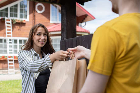Smiling beautiful woman customer receiving order from delivery man in front of house, Fast delivery Online delivery service concept, delivery home, e-commerce, shipping, online shopping food orderの写真素材