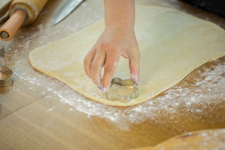 womans hand slices sheet of dough with cookie mold for homemade cookies in kitchen Ñookery class...