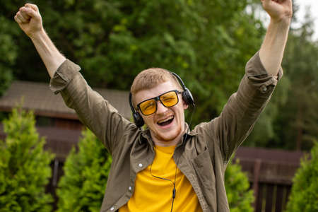 Joyful smiling man in headphones listen positive music with closed eyes, nature background. Summer...