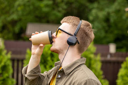 Portrait of young bearded guy in yellow glasses and yellow t-shirt casually dressed sipping coffee...