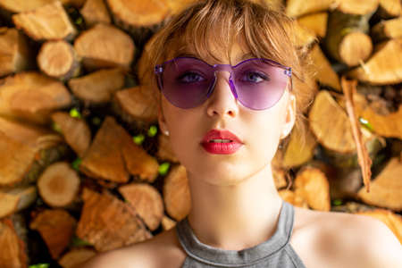 Portrait of  brunette girl in sunglasses with brightly colored lips, posing shoulders open against background of firewood stack looking at camera. glamorous lady in countrysideの写真素材