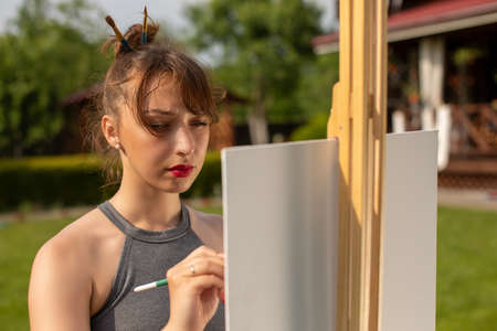 attractive brunette girl paints easel painting at her country house. Summer colours concept Creativity conceptの写真素材