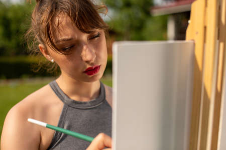 Close up portrait of young beautiful woman female artist painting picture on canvas outside on loan in park, outdoors relaxing activity, creative hobby, creation, inspiration conceptの写真素材