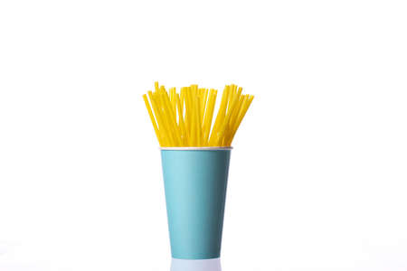 Yellow plastic drinking straws in blue disposable paper cup isolated on white background. Cafe, fun...