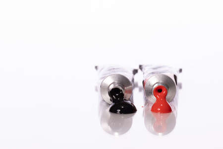 Two squeezed acrylic paint tubes red and black colours reflected in table surface isolated on white...