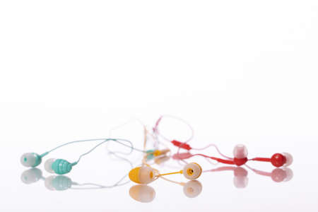 bunch of small colorful earphones reflected in glass table surface on white background green, yellow, red color. traffic light concept close up. do not use headphones while driving conceptの写真素材