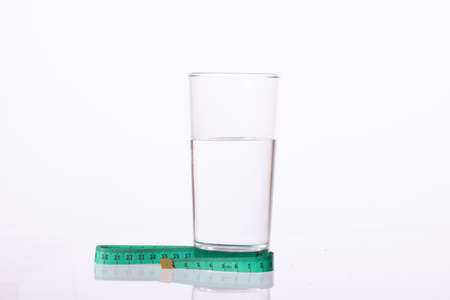 Green measuring tape and transparent glass of water isolated on white background. Diet, sport,...