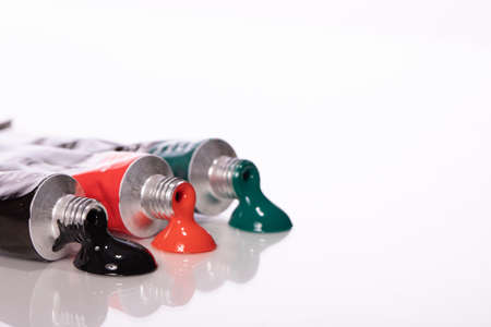Three squeezed acrylic paint tubes green, red and black colours reflected in glass table surface...