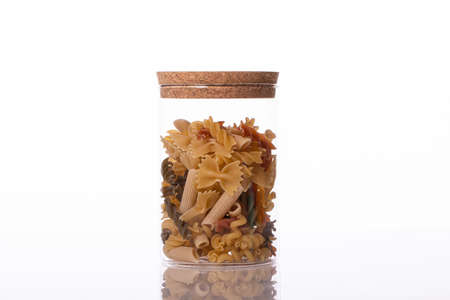 Various raw pasta in transparent jar isolated on white background. Mix of penne, fusilli, farfalle. Italian restaurant, food industry, diet, healthy food, high calorie, recipes concept. Copy spaceの写真素材