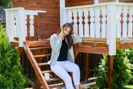Young beautiful woman resting outdoors on porch of country house, businesswoman talking on mobile...