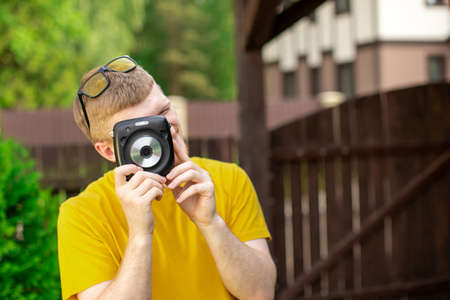 Young creative handsome man in yellow casual wear having fun outdoors, takes photo with instant...