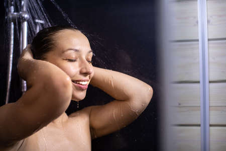 Happy beautiful woman standing under stream of hot water in bathroom, taking shower. Lifestyle, beauty, personal care, shower systems, relaxing time, young smiling lady enjoying showering, copy spaceの写真素材