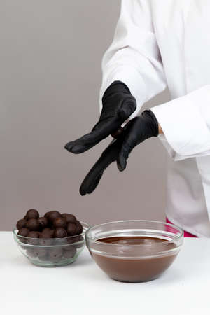 Close-up chocolatier in white uniform making hand-crafted dark chocolate truffles, preparing delicious handmade chocolate candies, rolling truffle between palms forming round shape, confectioneryの写真素材