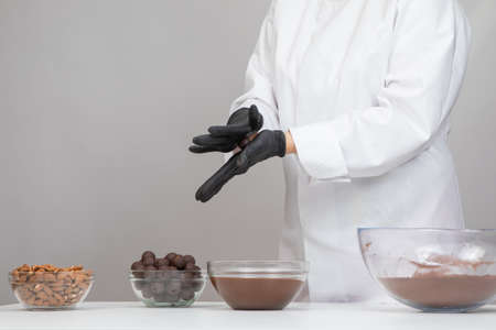 Chocolatier in white uniform step-by-step making hand-crafted dark chocolate truffles, preparing delicious handmade chocolate candies, rolling truffle between palms forming round shape, confectioneryの写真素材