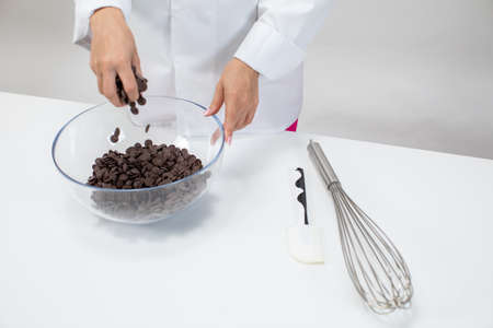 Closeup female chef pours dark chocolate drops chips morsels callets isolated on white background....