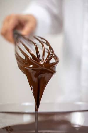 Closeup pouring tasty dark melted couverture chocolate on whisk isolated on white background. Chocolatier making premium hand-crafted chocolate. Candy making, pastry bakery production, dessert conceptの写真素材