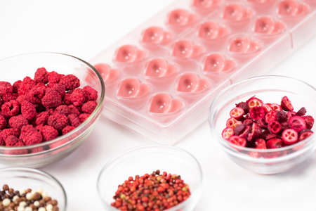 Heart shape confectionery mold with organic melted ruby chocolate and natural dried red berries species filling, hand-crafted premium homemade candies. Chocolate production, candymaking conceptの写真素材