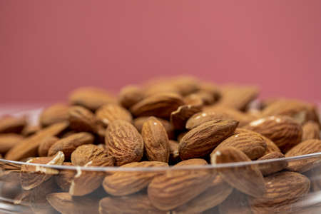 Closeup raw peeled almonds in glass bowl on pink background, organic fresh nuts, natural delicious...