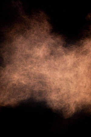 Flying cocoa powder on isolated black background, brown chocolate dust cloud. Creative sweet hurricane storm tornado concept, copy text space. Dark sand abstract screensaver, explosion burst textureの写真素材