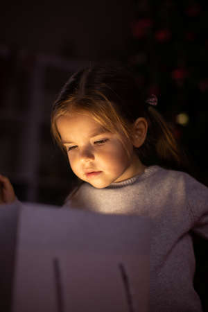 Christmas miracle concept, cute toddler girl peeks into magic gift box on Xmas eve. Dark backdrop....