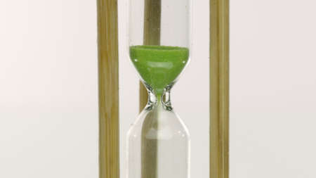 Close up hourglass countdown isolated on white background. Light green sand falling move through...