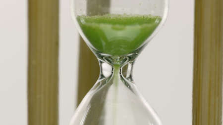 Close up hourglass countdown isolated on white background. Light green sand falling move through...