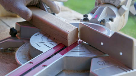 woodworker cuts oak wooden workpiece diagonally at angle 30 degrees with mitre saw close-up....