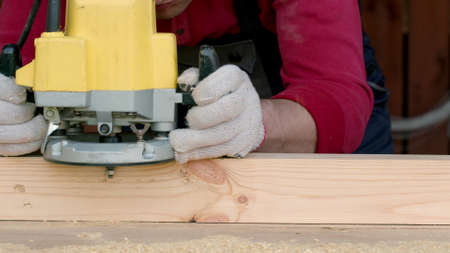 Caucasian carpenter processes wood beam with a milling machine in his carpentry workshop. The master...