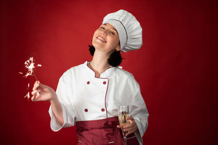 smiling attractive sexy female chef celebrating Christmas and New Year with glass of champagne and Burning sparklers looking at camera copy space. shift is over, new year come. Cook Christmas conceptの写真素材