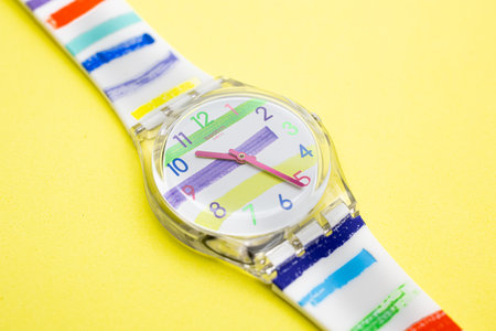 Rome, Italy 07.10.2020 - Swatch trendy fashion swiss made quartz watch isolated on yellow background close up. transparent plastic case striped design, youth hipster style watch for bright image.のeditorial素材