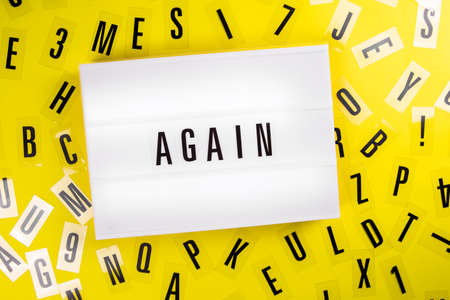 Again word writing on lightbox on scattered letters background of plastic alphabet. Second and third wave of  pandemic, lockdown concept. Trouble repeating, crisis returningの写真素材
