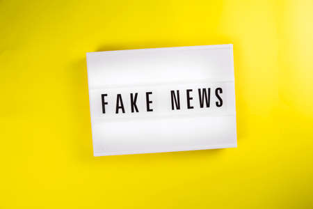 Fake News text on lightbox on yellow background isolated. vintage billboard Top view, flat lay. Information noise, political propaganda, misinformation, non-confidential sources of information conceptの写真素材