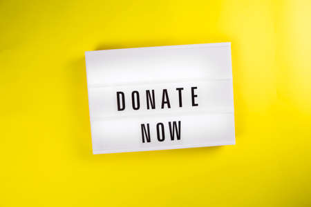 Donate Now text on lightbox on yellow background isolated. Top view, flat lay. Announcement of charitable foundation, call for donations, compassion, money transfers to charity organizations conceptの写真素材