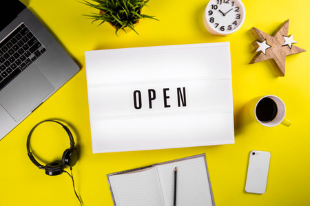 Open word on lightbox on modern yellow office desktop with laptop, smartphone, coffee mug, notebook. quarantine opening, isolation end concept. Open cafe, exhibition, office center conceptの写真素材