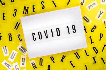 Lightbox with text COVID 19 on yellow background with black letters randomly scattered. Concept of coronavirus pandemic, worldwide lockdown, medical research news, vaccination, analytics, statisticsの写真素材