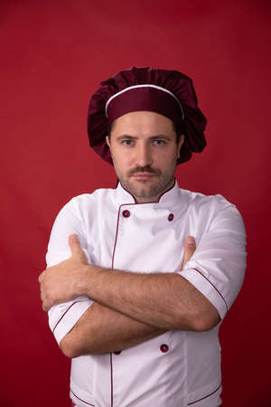 Portrait of handsome chef in uniform looks at camera on red background