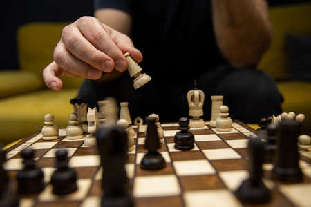Hand taking next step on chess game. Human hand moving wooden dark bishop pieceの写真素材