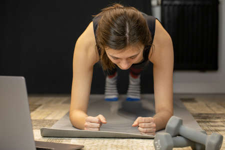 Young woman does abs exercise, enjoys bodybuilding training stands in plankの写真素材