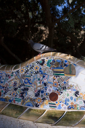 Barcelona, Spain, May 1, 2020 - pigeon sits on ceramic mosaics of bench in Guell Park. Broken ceramic tiles basis for pictorial mosaic. concept of artists union with natureのeditorial素材