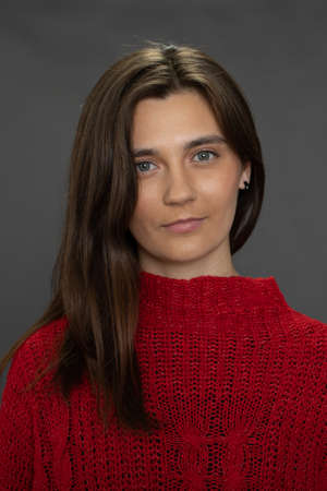 Young charming woman in red looks at camera on dark background, natural beautyの写真素材