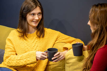 young lesbian couple talking on couch with cup of coffeeの写真素材