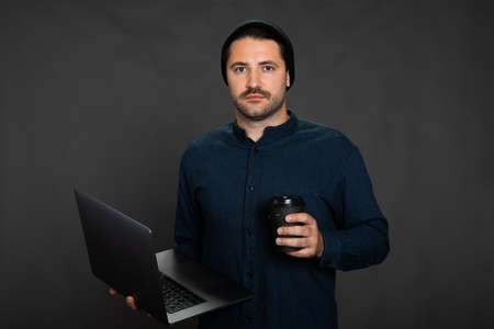 Stylish man on grey background with laptop and coffee, copy space, freelanceの写真素材