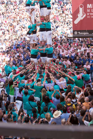 Tarragona, Spain, September 19, 2019 - Helmeted little Girl Climbing to Top of Human castells Tower. Childlike courage, emancipation concept. crowd of tourists watch erection of Castells human towerのeditorial素材